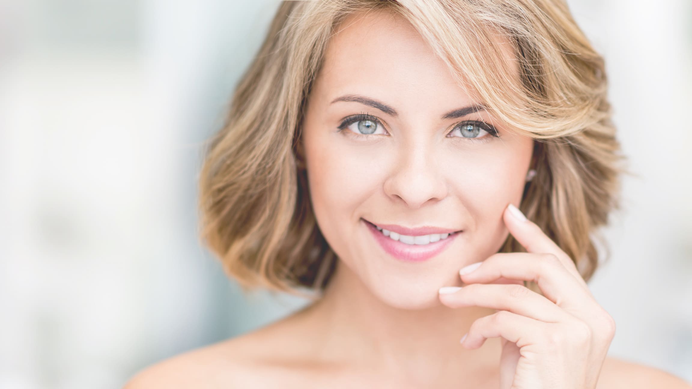 Model with a short blonde bob smiling, her hand at her cheek